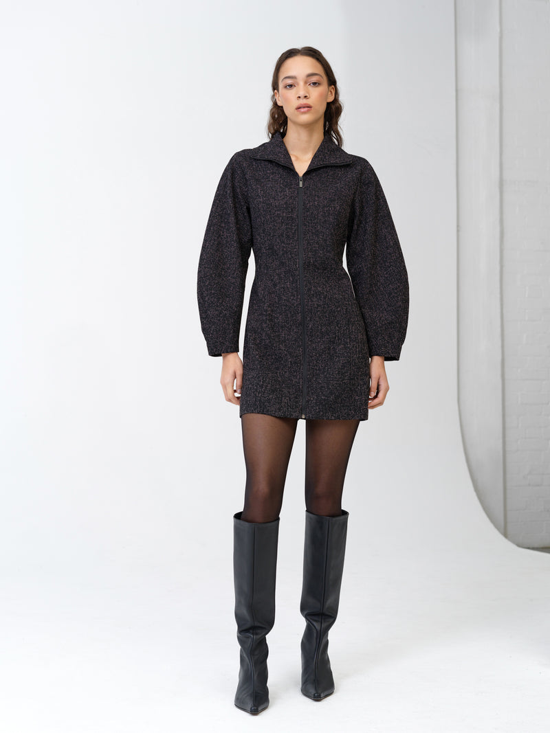 Woman wearing a black boucle mini dress with long banana sleeves and a zip through collar