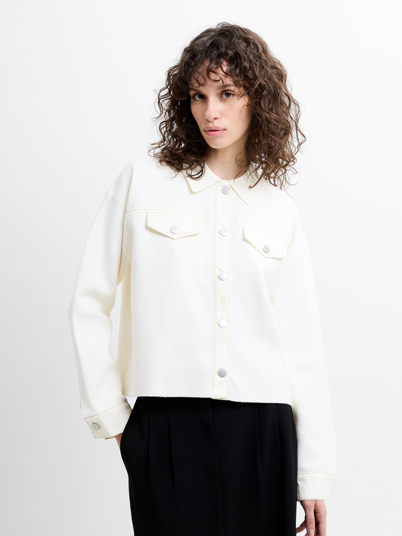 Woman wearing a cream knitted denim mix collared jacket with dropped long sleeves and a collar.